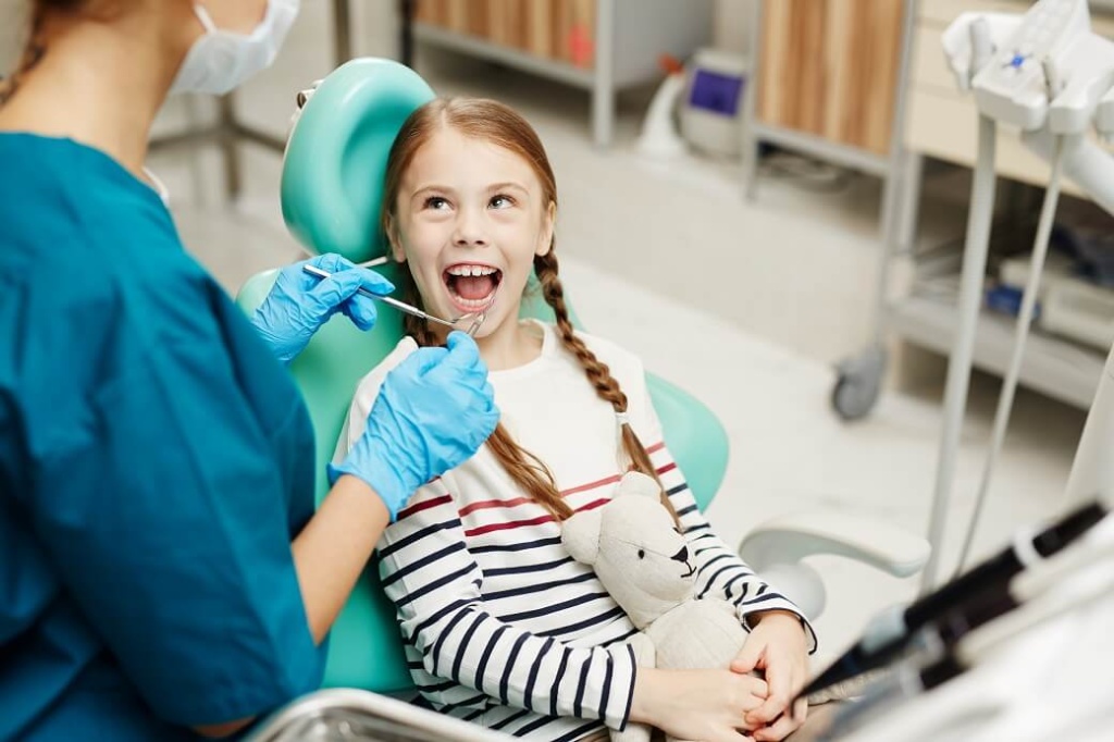 детский стоматолог осматривает рот девочки