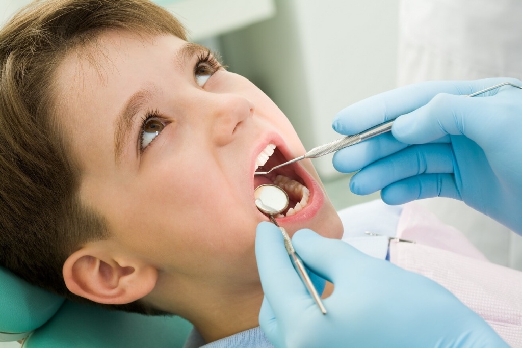 детский стоматолог осматривает зубы мальчика